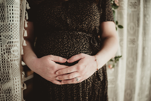 Pregnant woman with hands embracing abdomen