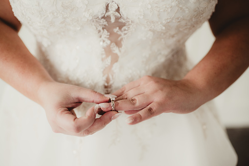 Bride in her wedding dress slipping wedding ring on her hand