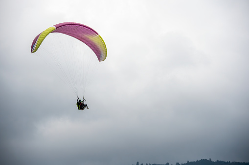 A tourist experiencing the thrill of paragliding in the mountains of Sikkim on the outskirts of Gangtok city.\n\nThis was photographed on a clear day on summer afternoon.