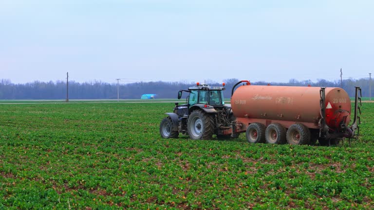 AERIAL Drone Shot of Water Tanker Driving on Agricultural Field Under Sky in Village