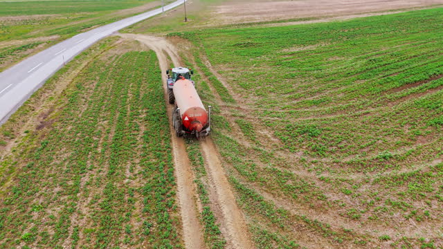 AERIAL Drone Shot of Tractor with Water Tanker Driving on Agricultural Field in Village