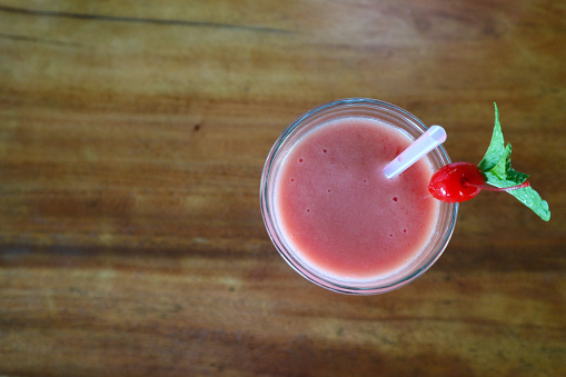 a glass of strawberry smoothie juice on a wooden table seen from above