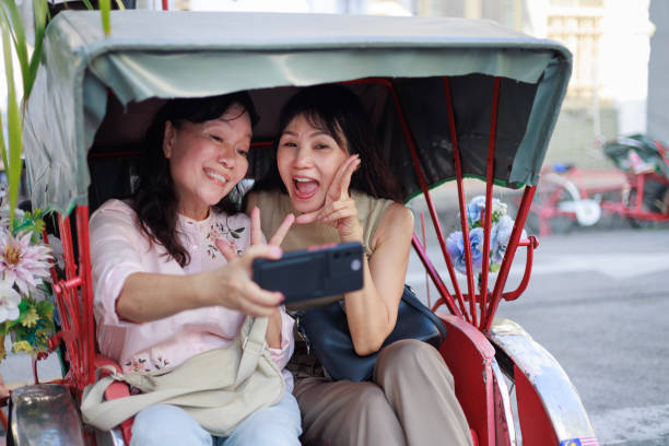 istock Joyful female travellers taking selfies using smartphone while enjoying a ride on a trishaw through the historic old town of Georgetown, Penang.