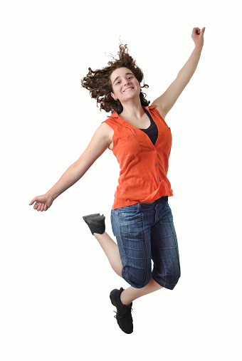 A joyful brunette woman jumps with her hair flying in the air against a white background, radiating happiness and energy.