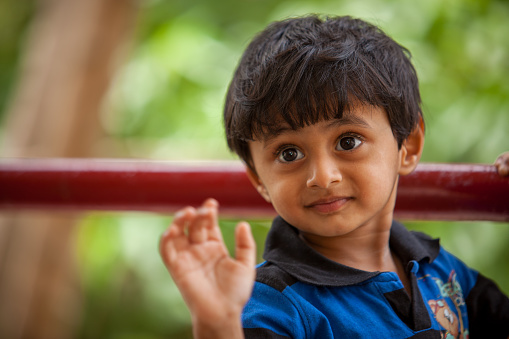 A toddler with wide eyes holds on to a red bar, looking curious with a green blurred background
