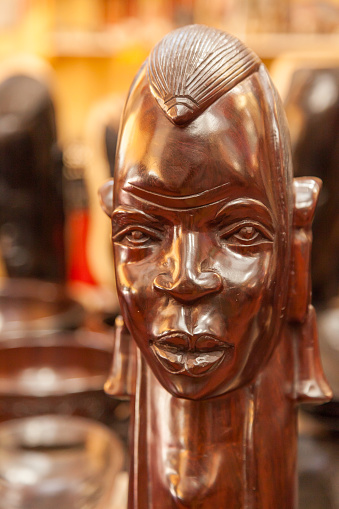 A wooden statue of a man with a mask on his face for sale in Kenya. The statue is brown and has a serious expression