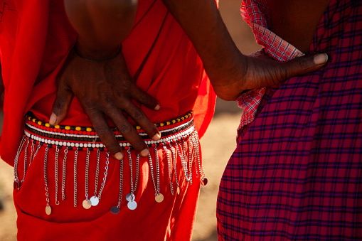 Two people wearing red and blue clothing. One of them has a necklace on. The necklace is made of beads and has a silver chain from folk dance tribal Kenya.