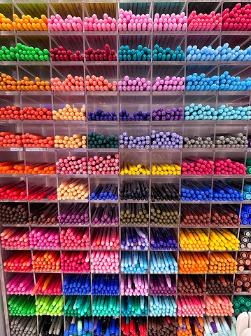 Stock photo showing wall mounted, shelving unit with pigeon holes containing a variety of multicoloured, felt tip pens for sale in a stationery store.