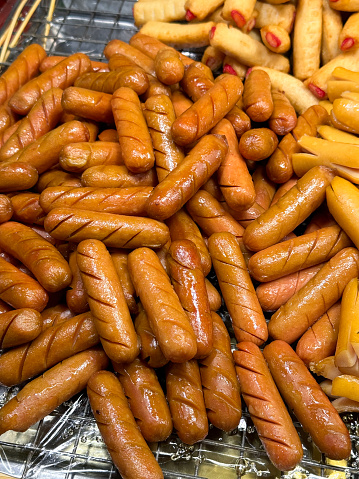 Stock photo showing close-up, elevated view of butcher's display tray containing a heap of precooked varieties of sausages ready for sale as snacks.