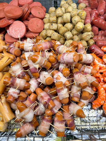 Stock photo showing close-up, elevated view of butcher's display tray containing a heap of precooked varieties of sausages and prawns ready for sale as snacks.