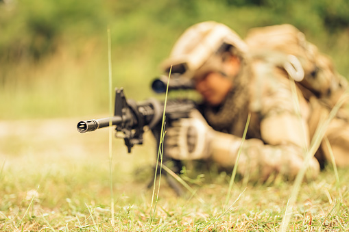 soldiers survey a jungle, carrying M16 rifles and pistols, wearing camouflage uniforms, military helmets and vision goggles