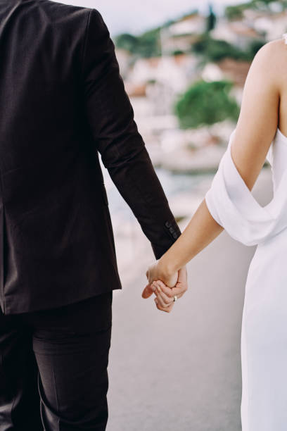 istock Bride and groom are standing holding hands on the road. Back view. Cropped 2070245802