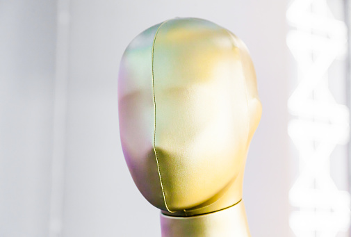 Mannequin head in golden-pink tones, on a light background with backlights
