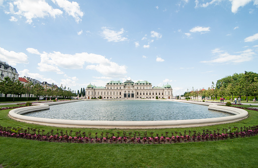 Vienna, Austria - June 12, 2013: Symmetric view of large pond surrounded by flower beds. Symmetric photo of 18th century baroque palace behind the pond.