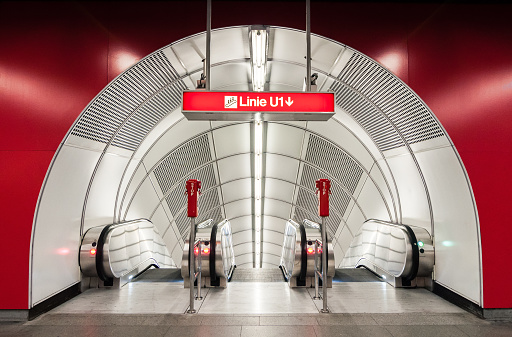 Subway station escalators. Entrance from hall with red walls into empty white tunnel with three moving staircases. Symmetric view of arch-shaped underground station escalator tunnel.