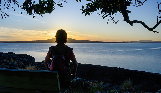 Woman enjoying the sunrise over the Rangitoto Island. Takapuna Beach. Auckland.
