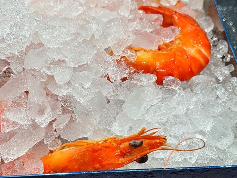 Stock photo showing close-up, elevated view of crate of freshly cooked king prawns in crushed ice, which is keeping them chilled and fresh before being sold at the fish market fishmongers.