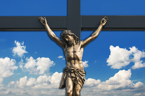 Crucified Jesus statue. Blue sky heaven. Christian cross symbol of faith.