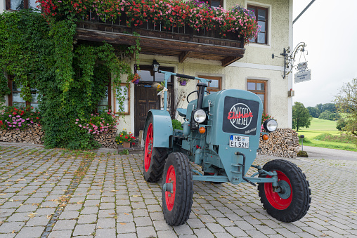 Eicher Diesel vintage tractor parked in front of the Lindl inn covered with blooming geraniums, Bavaria, Germany