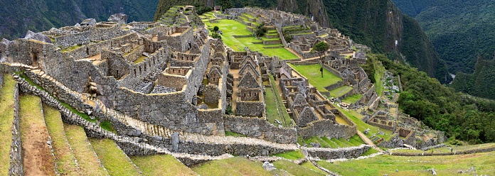Machu Picchu, Peru, November 12, 2021: Panoramic view of the Inca citadel Machu Picchu from 15th-century under low clouds. The ancient town is located in the Eastern Cordillera of southern Peru on a 2,430-meter (7,970 ft) mountain ridge and is listed as UNESCO World Heritage Site.