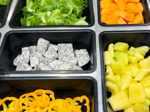 full frame image of hotel self service refrigerated buffet display, rows of salad bar trays of yellow bell pepper slices, dragon fruit (pitaya) pieces, lettuce leaves, cubed pineapple and mango, ingredients for self made salad, salad vegetable restaurant - refrigerator healthy eating mango fruit stock-fotos und bilder