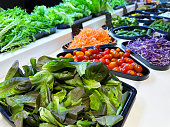 Close-up image hotel self service refrigerated buffet display, salad bar trays of lettuce leaves, cherry tomatoes, grated carrots, shredded red cabbage, mini cucumbers, broccoli florets, ingredients for self made salad, salad vegetable restaurant buffet