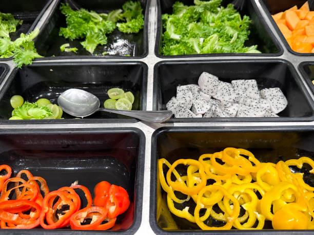 vollformatbild des selbstbedienungsbuffets des hotels, reihen von salatbar-tabletts mit roten und gelben paprikascheiben, drachenfruchtstücken (pitaya), weißen traubenhälften, salatblättern, gewürfelter mango, zutaten für selbstgemachten salat, salat - refrigerator healthy eating mango fruit stock-fotos und bilder