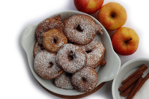 Deep fried apple rings with batter sprinkled with powdered sugar and cinnamon on white background