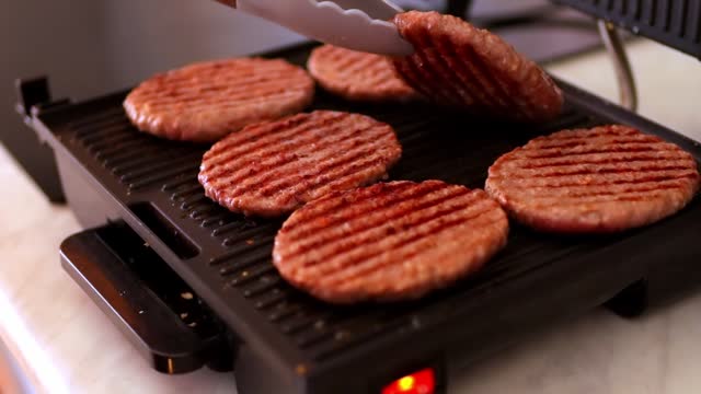 a woman fries hamburger patties on an electric grill. There is a grill in the kitchen. High quality FullHD footage