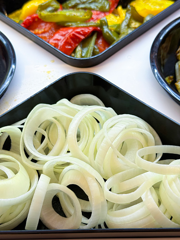 Stock photo showing close-up, elevated view of roasted red, green and yellow bell peppers and raw onion rings in plastic serving trays as part of hotel self service refrigerated buffet display.