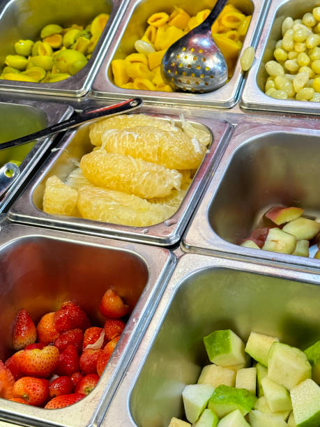 istock Full frame image of hotel self service refrigerated buffet display, fruit salad bar metal trays of  peeled and chopped tropical fruits, jackfruit, rambutan, pomelo, red and green apples, strawberries, ingredients for self made fruit salad, elevated view 2070570036