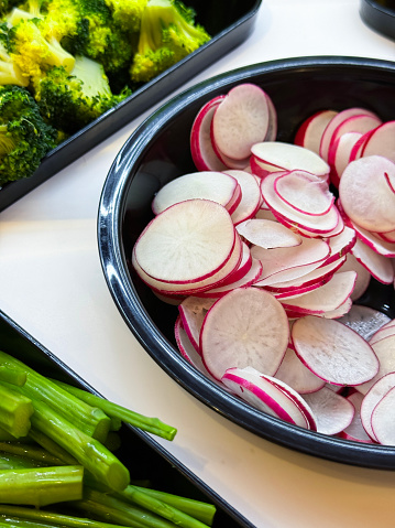 Stock photo showing close-up, elevated view of broccoli florets, radish slices and green beans in plastic serving trays as part of hotel self service refrigerated buffet display.