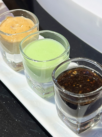 Stock photo showing close-up view of a row of three mini glasses containing salad dressings and dipping sauces.