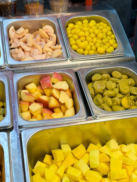 Close-up image of hotel self service refrigerated buffet display, fruit salad bar metal trays of peeled and chopped tropical fruits, rambutan, mango, pineapple, papaya, ingredients for self made fruit salad, elevated view