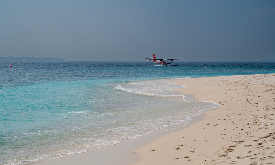 A nice sea coast with a sandy beach and a seaplane on the surface. Sunny weather.