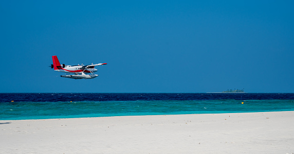 Seaplane is flying low above sea level by the sandy beach. Blue sky.