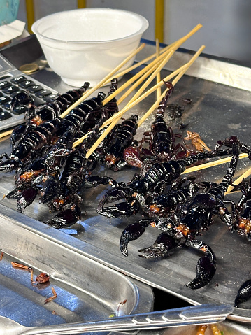 Stock photo showing close-up, elevated view of a heap of deep-fried invertebrate kebabs of scorpions on bamboo skewers being sold at street food market stall.