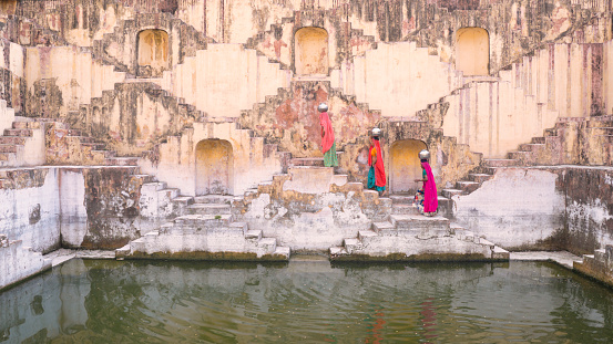 Indian women carrying water from stepwell near Jaipur, Rajasthan, India. Women and children often walk long distances to bring back jugs of water that they carry on their head.