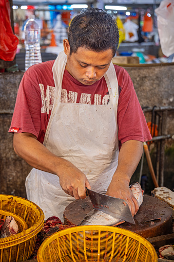 Chow Kit market, Kuala Lumpur, Malaysia - January 8th 2024:  Male fishmonger cutting up a fish at a stall in the famous food market in the center of the capital