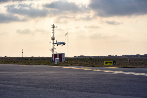 An airplane on final approach flying past airport ground navigational aids.