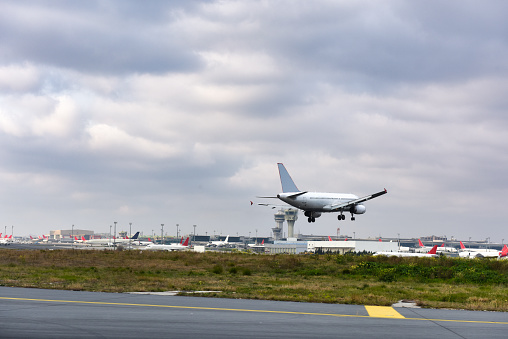 A jet nearing touchdown with an array of parked aircraft at the airport and control towers in the background.