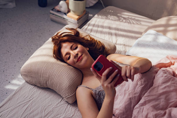 istock Young Woman Relaxing in Bed with Smartphone, Morning Light 2070690759