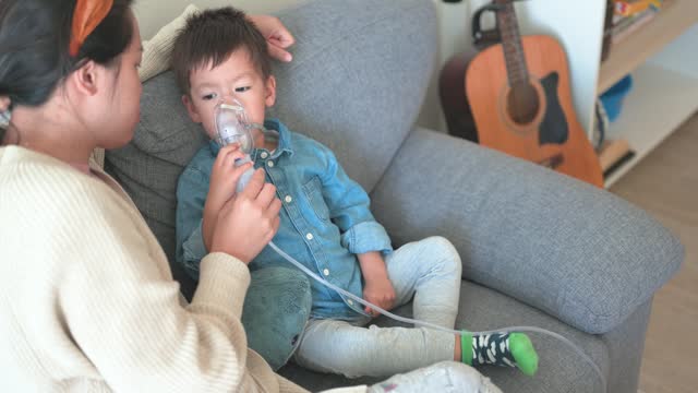 Child receiving medical inhalation treatment at home with moms help