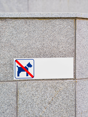 This sign, attached to a gray stone wall in Sweden, clearly indicates that the area is off-limits for dog walking or resting. The blue and white sign features the universally recognized symbol of a dog within a red circle and a diagonal line indicating prohibition, accompanied by Swedish text stating that the resting of dogs is forbidden.