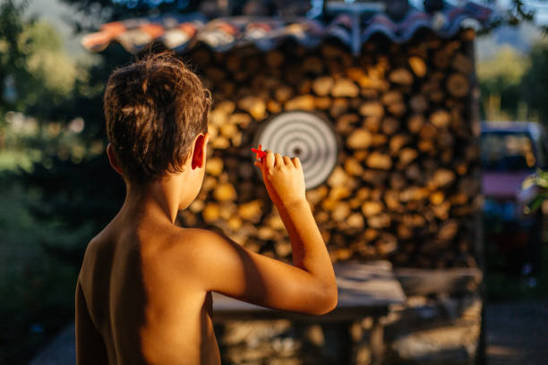 Teenage boy throwing darts on a dartboard, having fun in the yard on a hot summer day