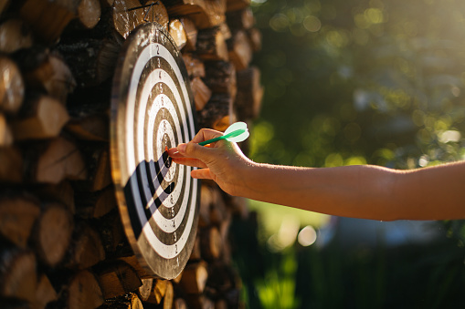 Teenage’s hand pointing with dart on a dartboard in the yard
