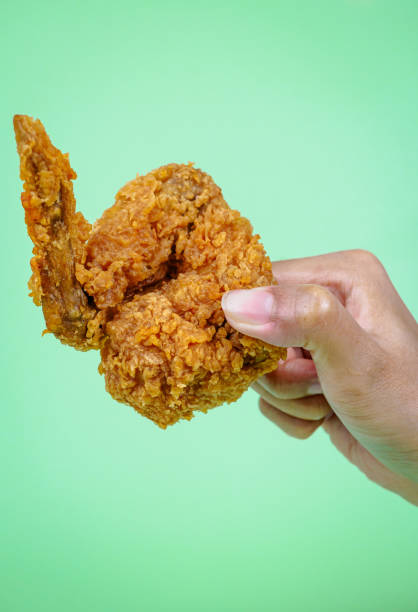 istock Female hand holding fried chicken on green background. 2070897340