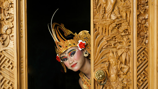 balinese girl wearing Balinese traditional dress with crown, jewelry, and gold ornament accessories sticking out of the door