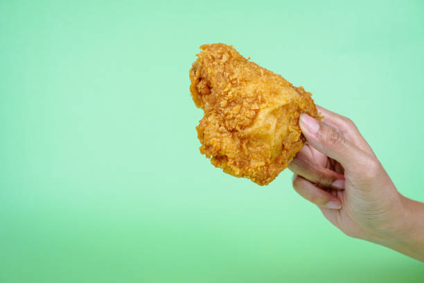 istock Female hand holding fried chicken on green background. 2070903699