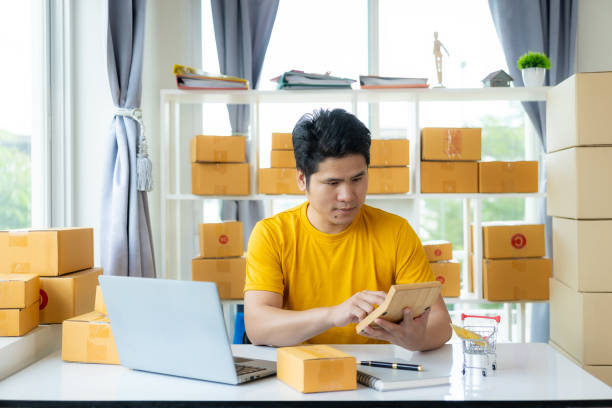 istock small business owner Asian man using mobile app on smartphone is checking parcel boxes, doing retail, parcel delivery, SME, online shopping. 2070917219